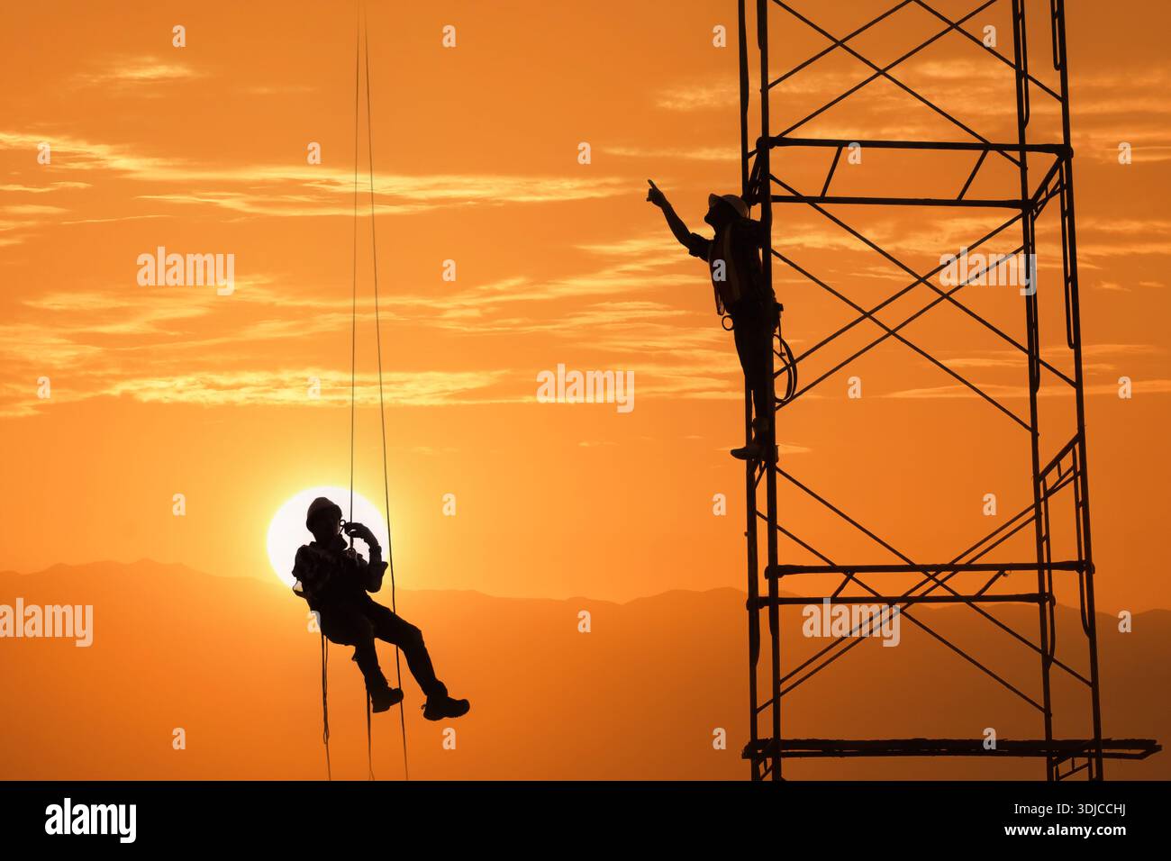Silhouette di un operaio edile appeso in un'imbracatura con un'altra persona in piedi su acciaierie strutturali al tramonto, Thailandia Foto Stock