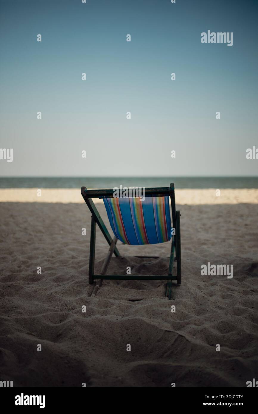 Una singola sedia da spiaggia si erge da sola sulla spiaggia sabbiosa, di fronte al mare tranquillo, simboleggiando la solitudine, la solitudine e i momenti tranquilli vicino all'oceano. Foto Stock
