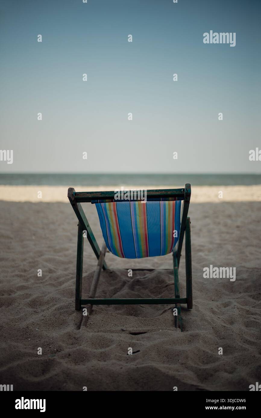 Una singola sedia da spiaggia si erge da sola sulla spiaggia sabbiosa, di fronte al mare tranquillo, simboleggiando la solitudine, la solitudine e i momenti tranquilli vicino all'oceano. Foto Stock