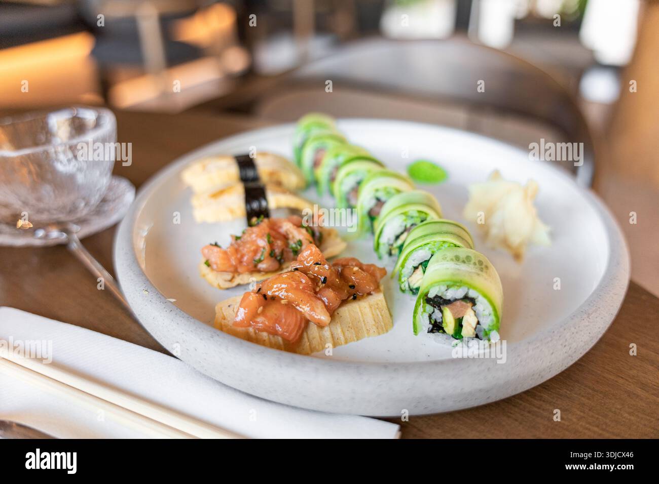 Un piatto di sushi con nigiri di salmone e involtini di cetriolo. Il piatto è servito con zenzero sottaceto e wasabi, adagiato su un tavolo di legno. Foto Stock