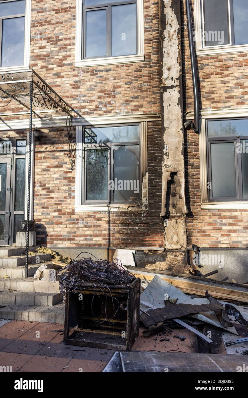 La striscia verticale carbonizzata sulle pareti in mattoni segna il percorso del fuoco; la finestra rotta, l'armadio bruciato e i fili aggrovigliati si trovano tra i detriti in ambienti urbani danneggiati. Foto Stock