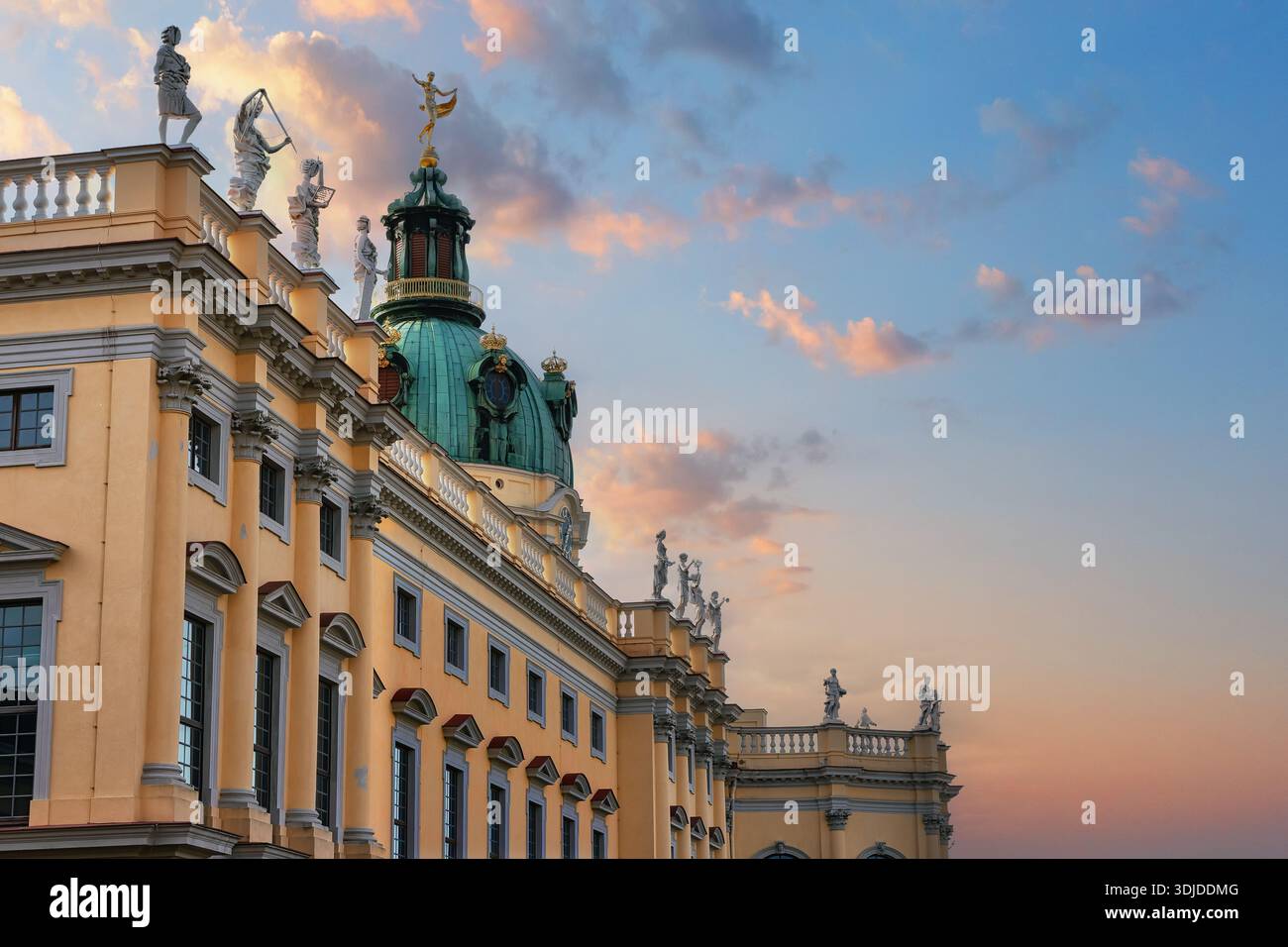 Facciata del palazzo barocco decorata con statue scolpite, pareti color pastello e cupola verde in rame che si illumina al tramonto, incorniciata da morbide nuvole e tiepida vita serale Foto Stock