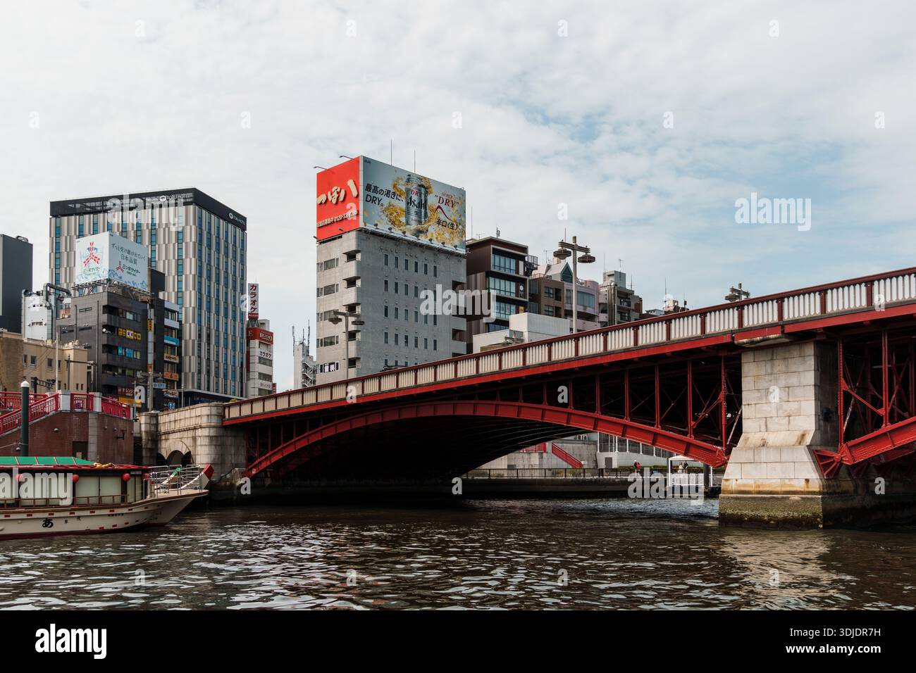 Tokyo, Giappone - 6 agosto 2024: Una vista panoramica di un ponte rosso sul fiume Sumida a Tokyo, con edifici e una barca in primo piano. Foto Stock