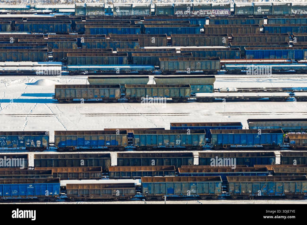 Vista aerea di un vasto deposito ferroviario pieno di file di vagoni ferroviari blu arrugginiti che poggiano su un terreno polveroso di neve, Warszawa, Województwo mazowieckie, Polonia. Foto Stock