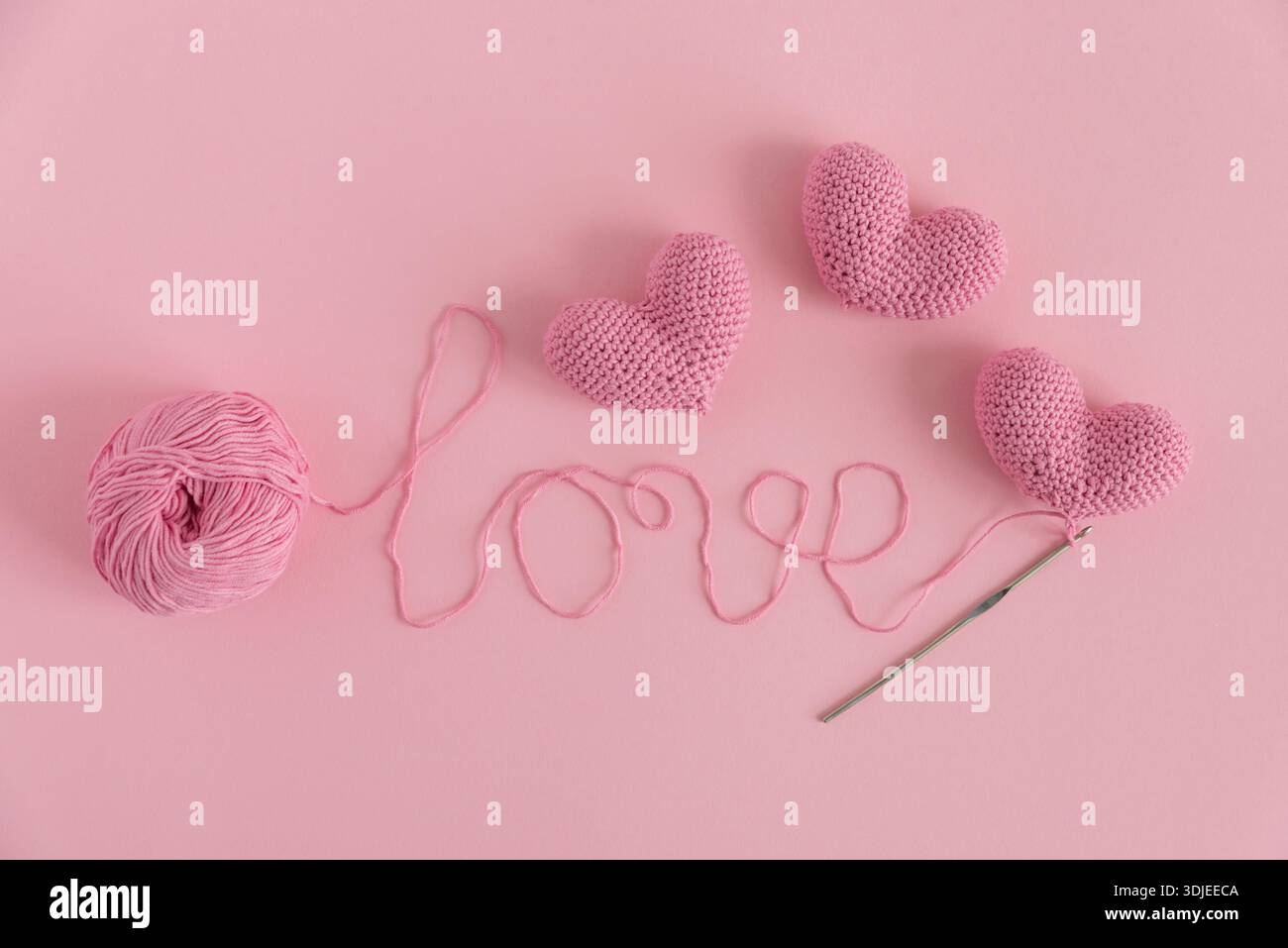 Cuori a crocchetto e amore spelling in filato. Piatto artigianale realizzato a mano su sfondo rosa Foto Stock