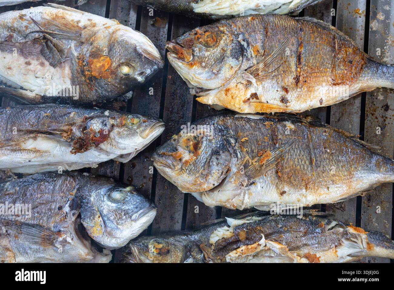 Una fila di pesce intero grigliato su un barbecue, con pelle croccante e segni di ciccioli. Scena di cucina all'aperto con un fascino rustico e saporito, adatto a se stesso Foto Stock