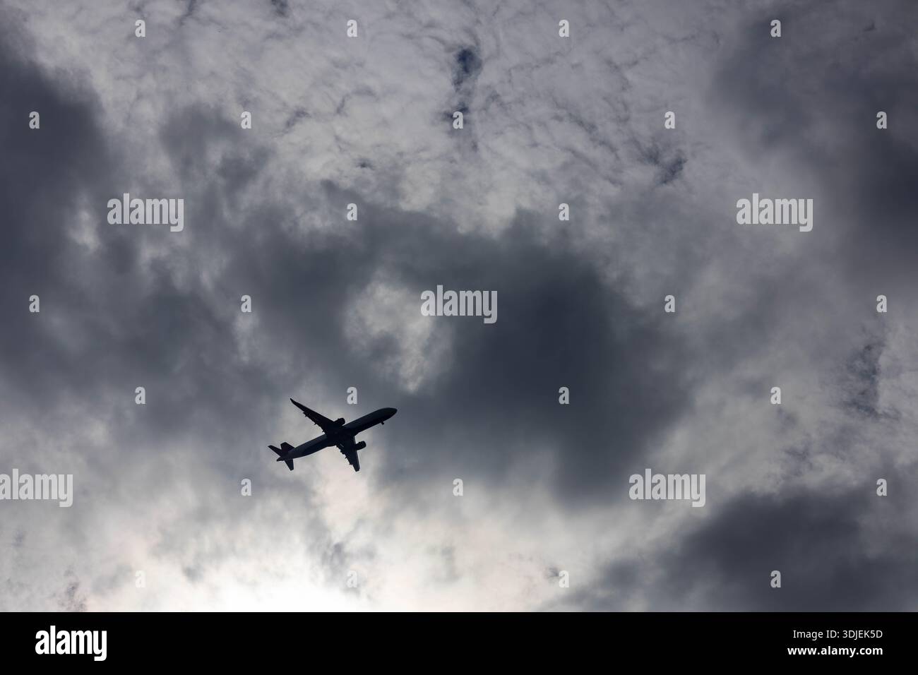 Una potente silhouette a basso angolo di un aereo passeggeri che attraversa un paesaggio nuvoloso e ad alto contrasto. Il sole è parzialmente oscurato dallo spessore, bi Foto Stock