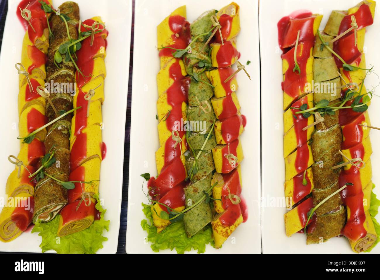 Crepes arrotolate assortite ripiene di ingredienti diversi, splendidamente guarnite con erbe, presentate su piatti bianchi, che mettono in risalto la creatività culinaria Foto Stock