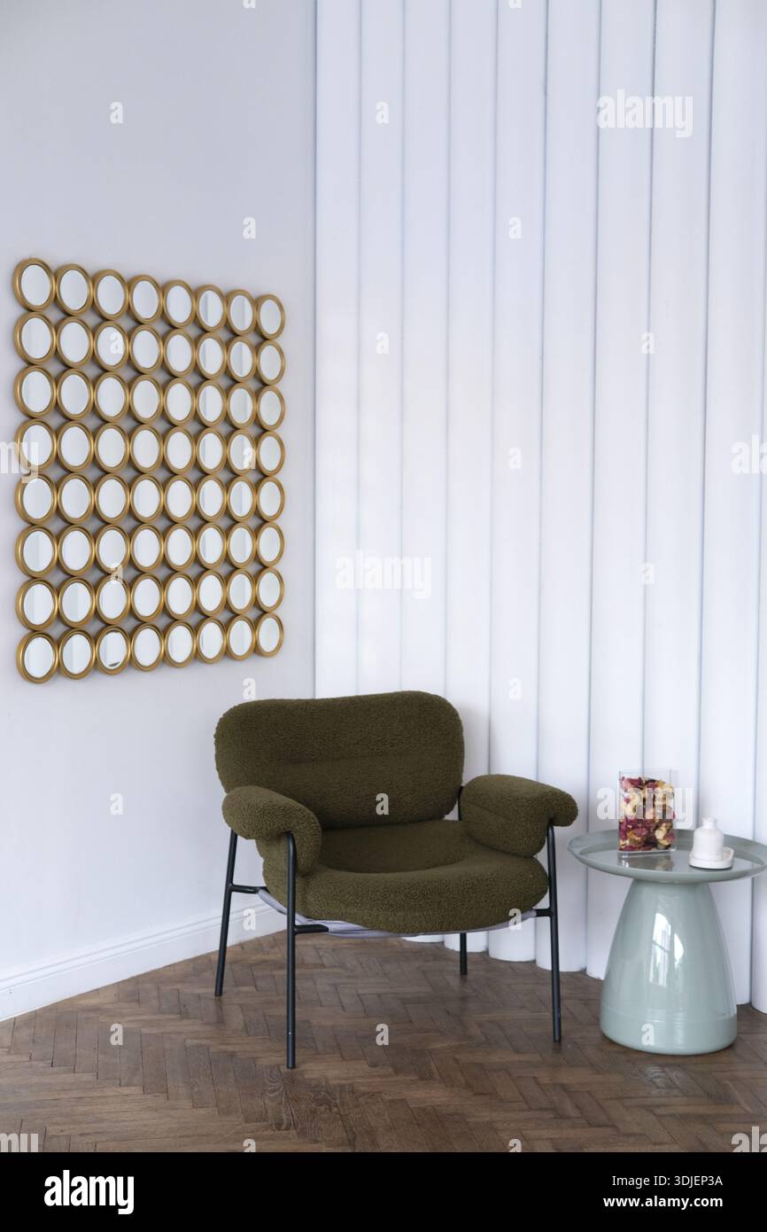 La poltrona verde è collocata accanto a un elegante tavolino laterale con elementi decorativi, adagiata su pannelli verticali bianchi e una disposizione distintiva degli specchi Foto Stock