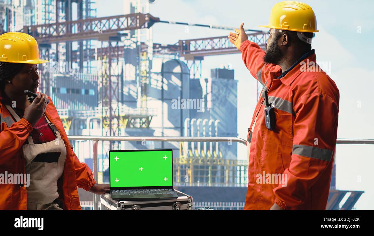 Computer portatile con schermo isolato utilizzato dai colleghi dell'equipaggio del carro di perforazione che tengono in mano un dispositivo radio per monitorare i sistemi. Team di progettazione sulla piattaforma offshore utilizzando walkie talkie e notebook Chroma Key Foto Stock