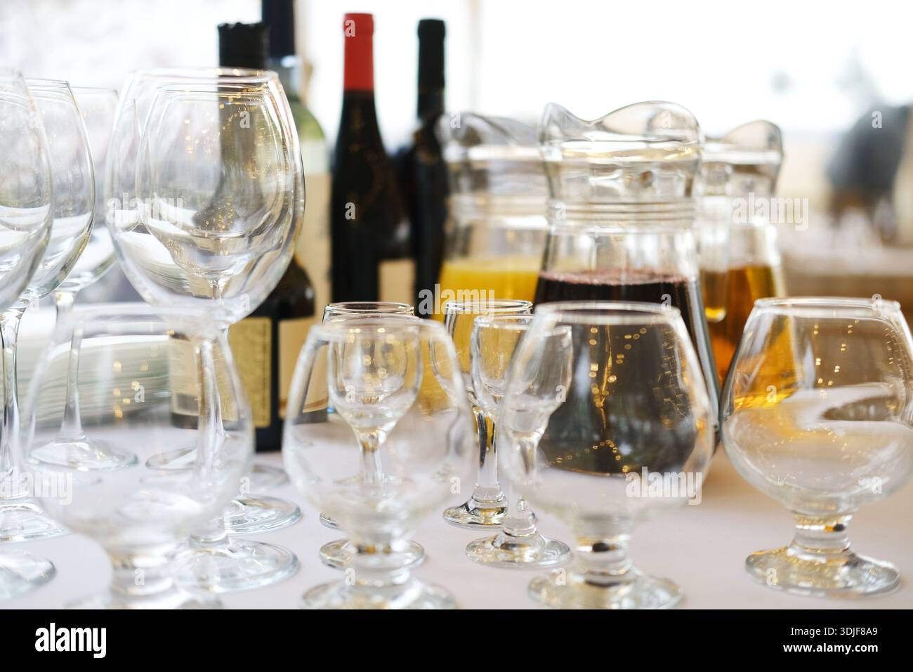 Vari bicchieri, tra cui bicchieri da vino e una caraffa piena di bevande, elegantemente disposti su un tavolo, creano un'atmosfera invitante per cenare Foto Stock