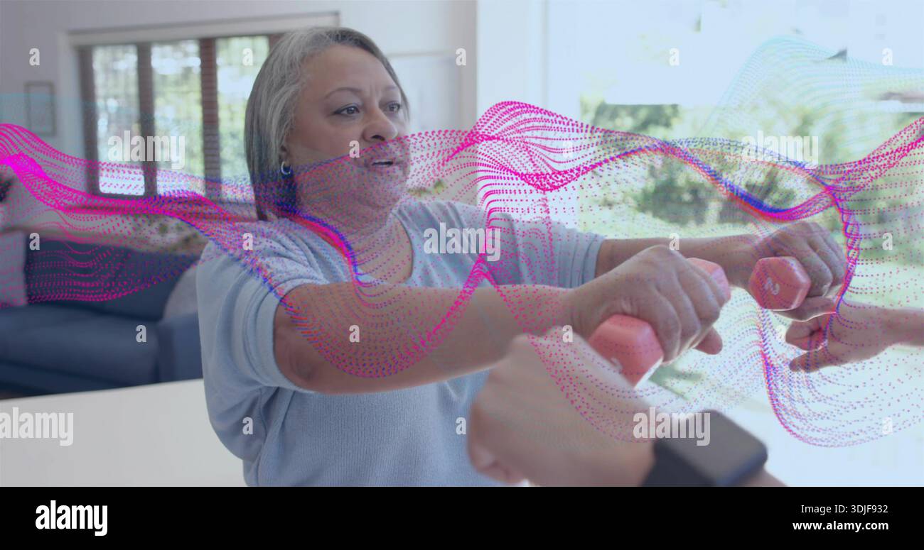 Con i manubri rosa, una donna anziana con la parte superiore blu che si estende al bancone di casa, una aiutante che mantiene il peso Foto Stock