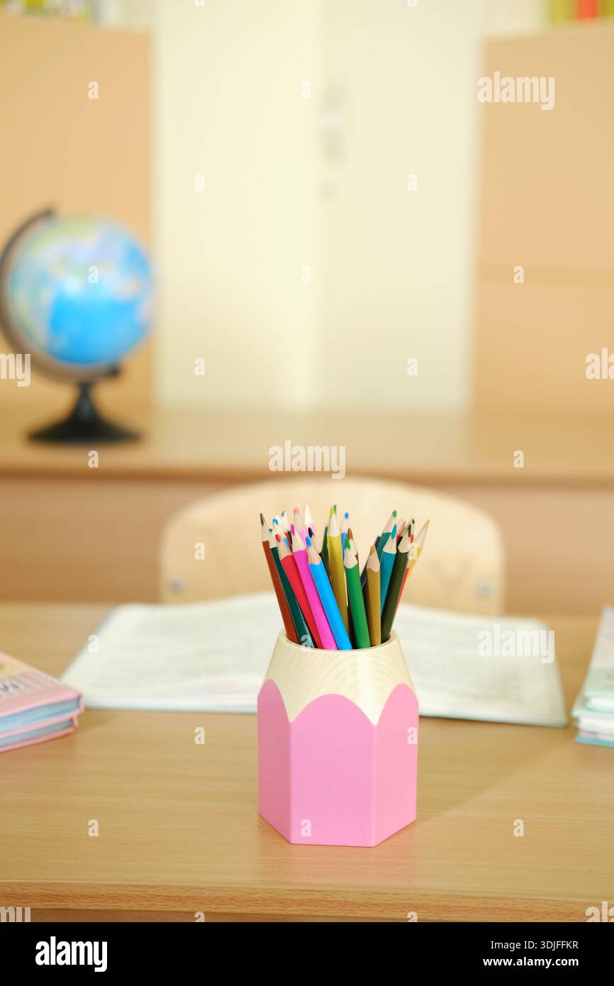 Matite dai colori vivaci in un supporto rosa su una scrivania in legno, circondate da materiali di studio e da un globo, creando un'invitante atmosfera educativa Foto Stock
