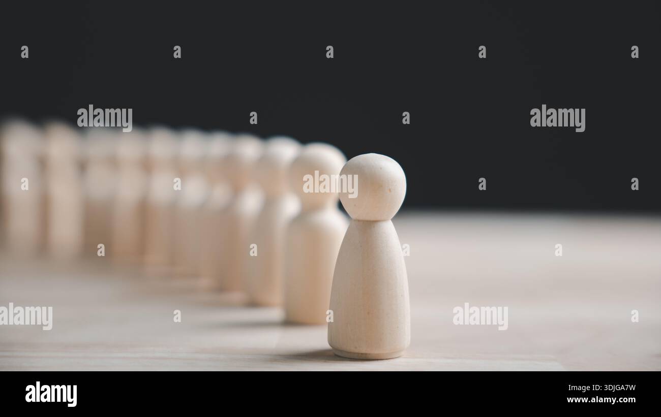 Una singola figura di legno si distingue da una fila di figure identiche su un tavolo di legno. Foto Stock