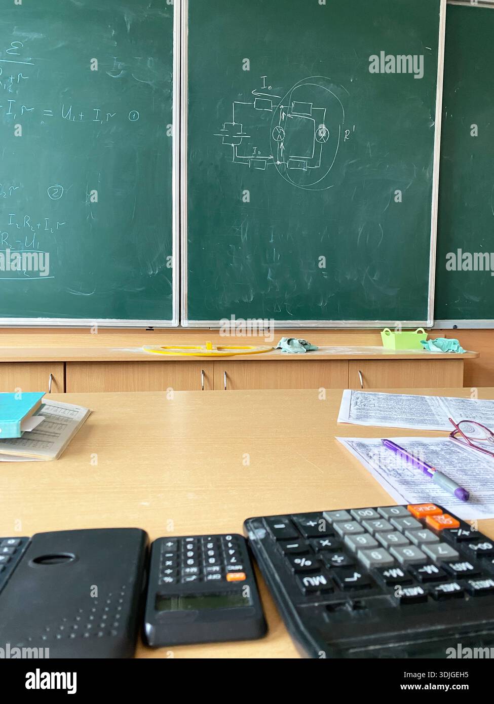 Ambiente educativo con una scrivania in legno che mostra calcolatrici e quaderni, mentre una lavagna mostra equazioni matematiche e diagrammi, enhanci Foto Stock