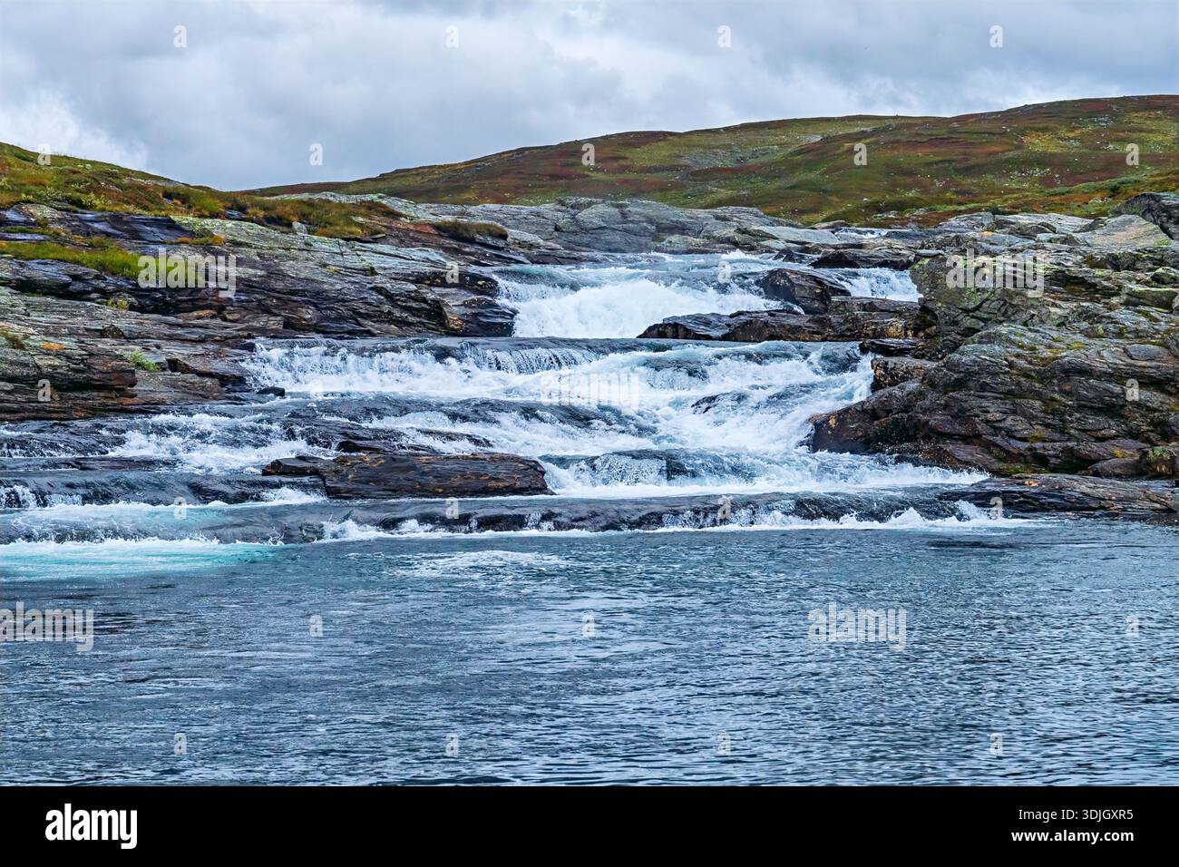 Il paesaggio di Vildmarksvagen raffigura un potente fiume che forma piccole cascate su numerose rocce scure, con vaste colline coperte da vegetazione sparsa Foto Stock
