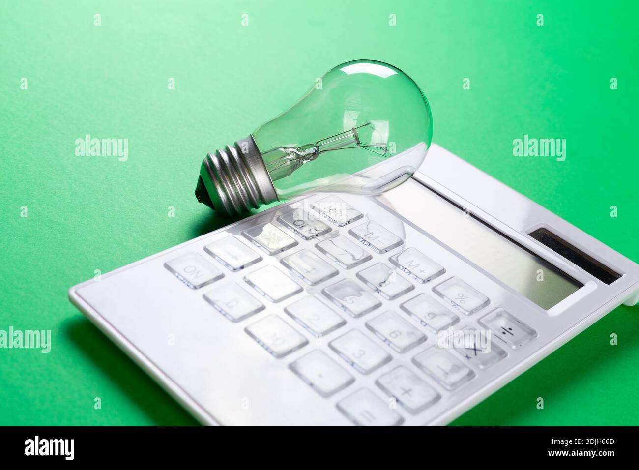 Calcolatrice con lampadina a incandescenza su sfondo verde. Piatto a risparmio energetico Foto Stock