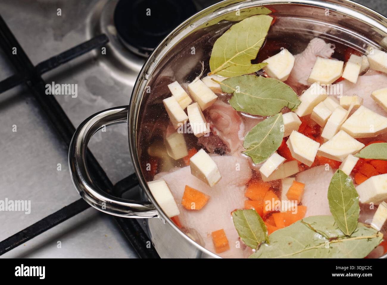 Cottura di zuppe fatte in casa su un piano cottura. Pentola con verdure e carne sospese nel brodo. Tradizionale processo di cucina casalinga. Cibo sano e confortevole. Foto Stock