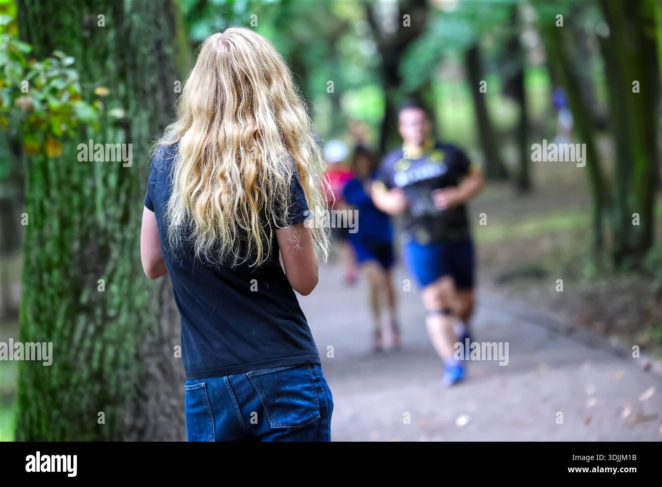 Persona dai capelli biondi che guarda i corridori in un lussureggiante parco verde Foto Stock