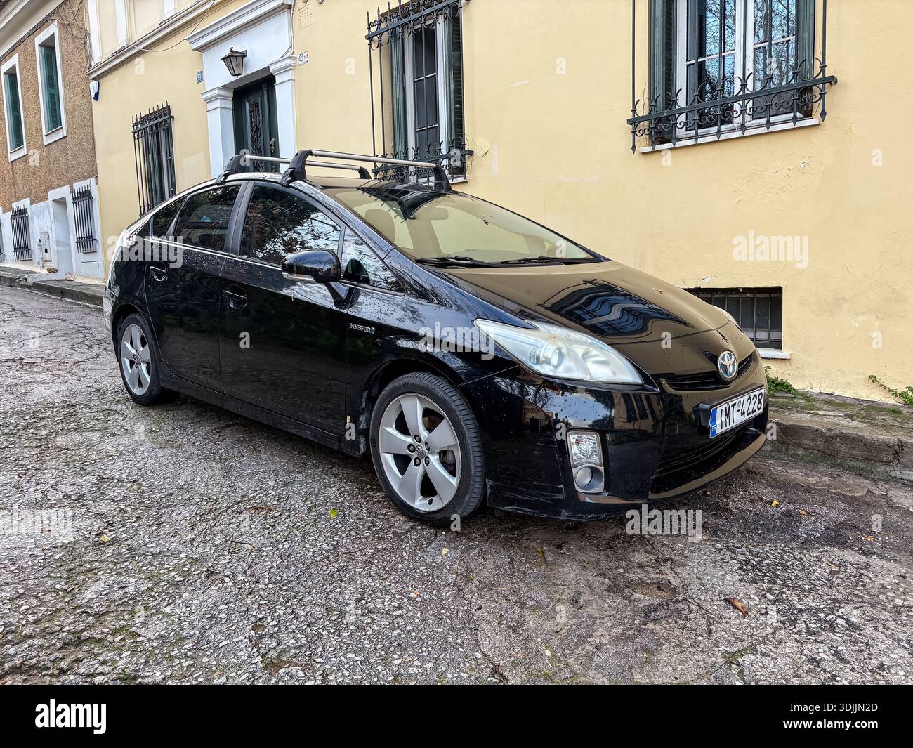 Toyota Prius nera / auto ibrida. Automobile, veicolo per pendolari. Parcheggiato su una strada sterrata e acciottolata nello storico quartiere Plaka di Atene, Grecia. Foto Stock