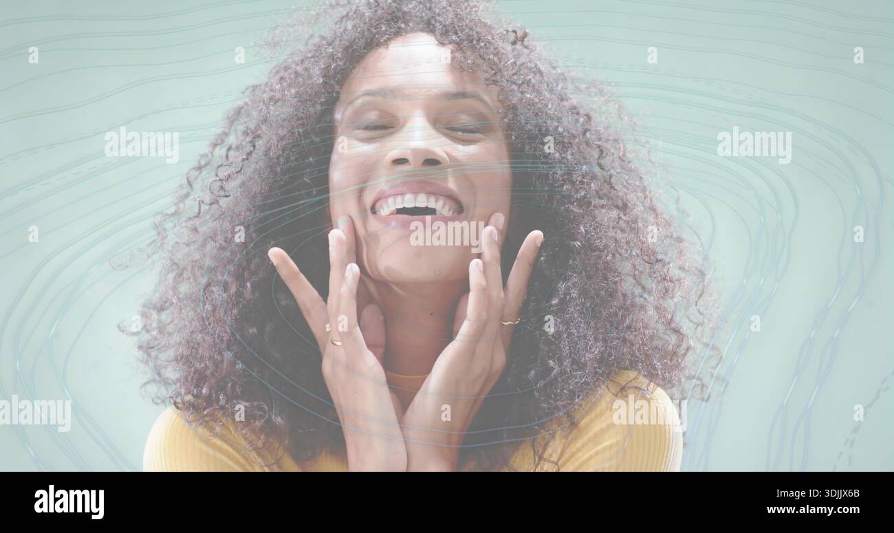 Donna sorridente che tocca il viso in studio, indossa un top di senape con anelli, collana e vortici digitali Foto Stock