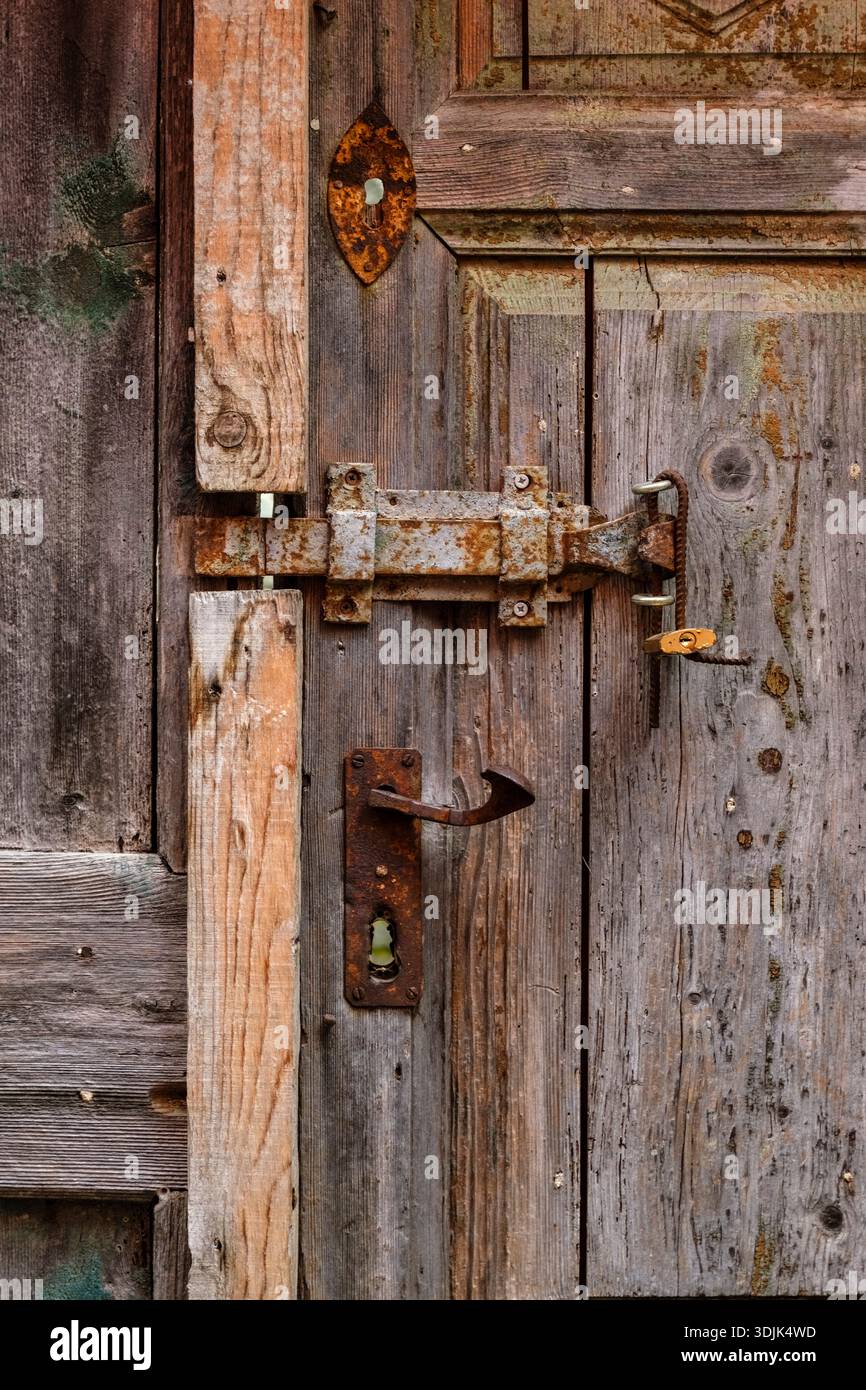Primo piano di una porta in legno resistente agli agenti atmosferici con una serratura in metallo arrugginito, un piccolo lucchetto giallo, una maniglia vintage e texture invecchiate. Foto Stock