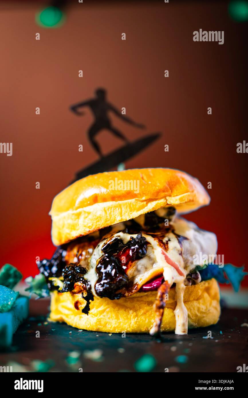 Delizioso hamburger di manzo con ricchi condimenti e un forte tema surf Foto Stock