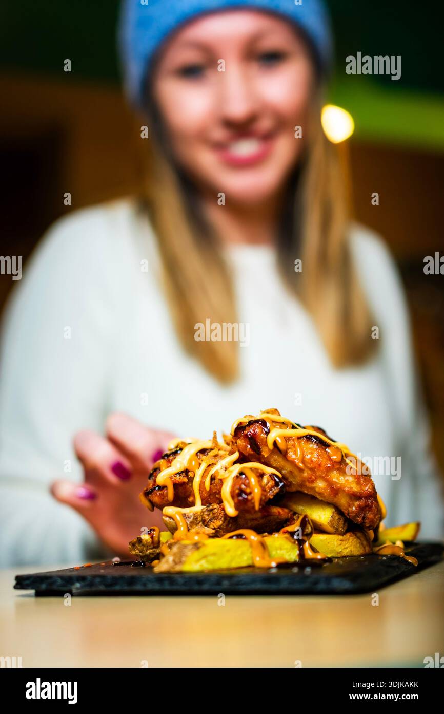 Donna in cerca di un gustoso piatto di ali di pollo e patatine fritte Foto Stock