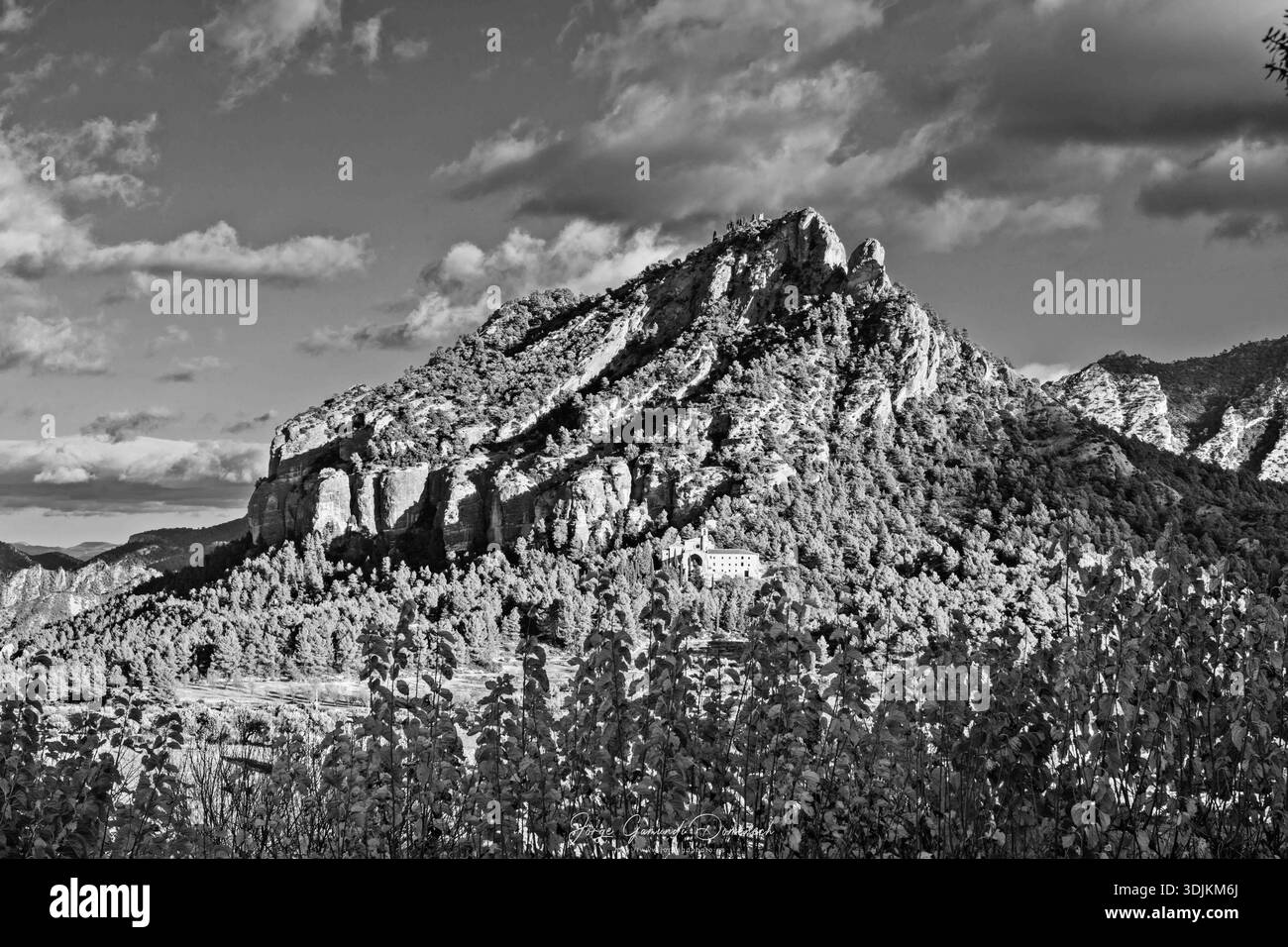 Una montagna con una casa sopra. La casa è in lontananza e la montagna è coperta di alberi Foto Stock