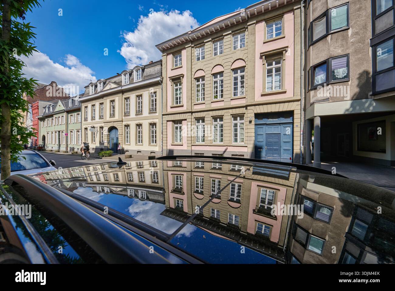 Edifici classici sulla strada Muelheimer Freiheit di Colonia, riflessi sul tetto di un'auto sotto un cielo estivo blu Foto Stock