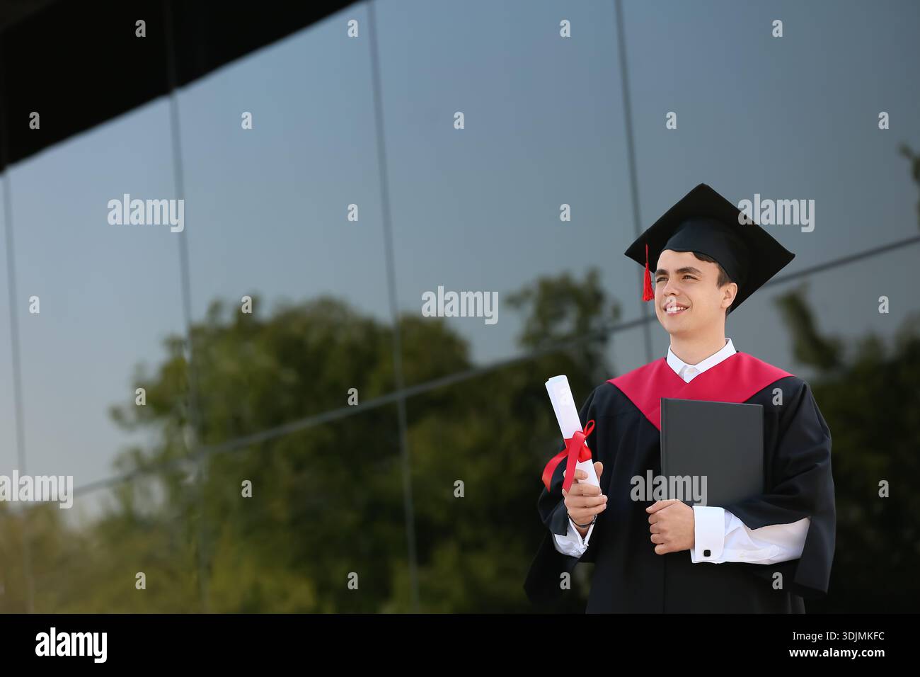 Studente laureato con diploma e libro vicino all'università Foto Stock
