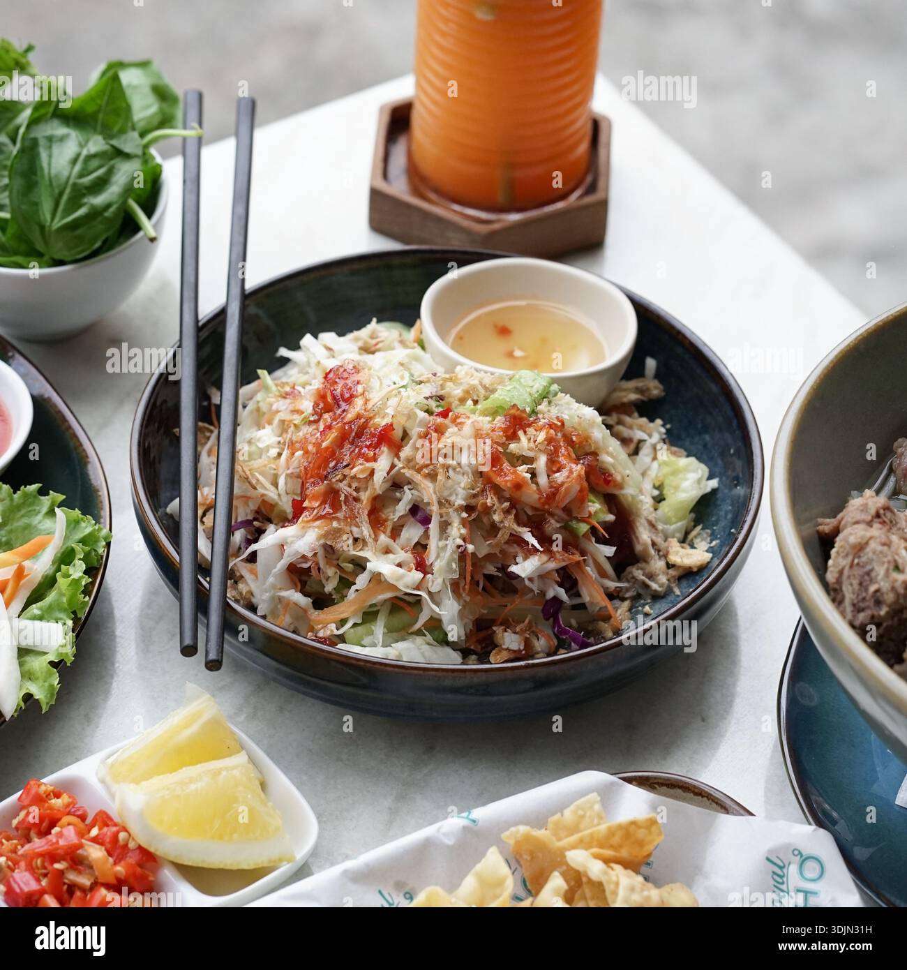 Insalata asiatica con erbe fresche, verdure e condimento piccante servita su un tavolo con vari accompagnamenti e condimenti. Foto Stock