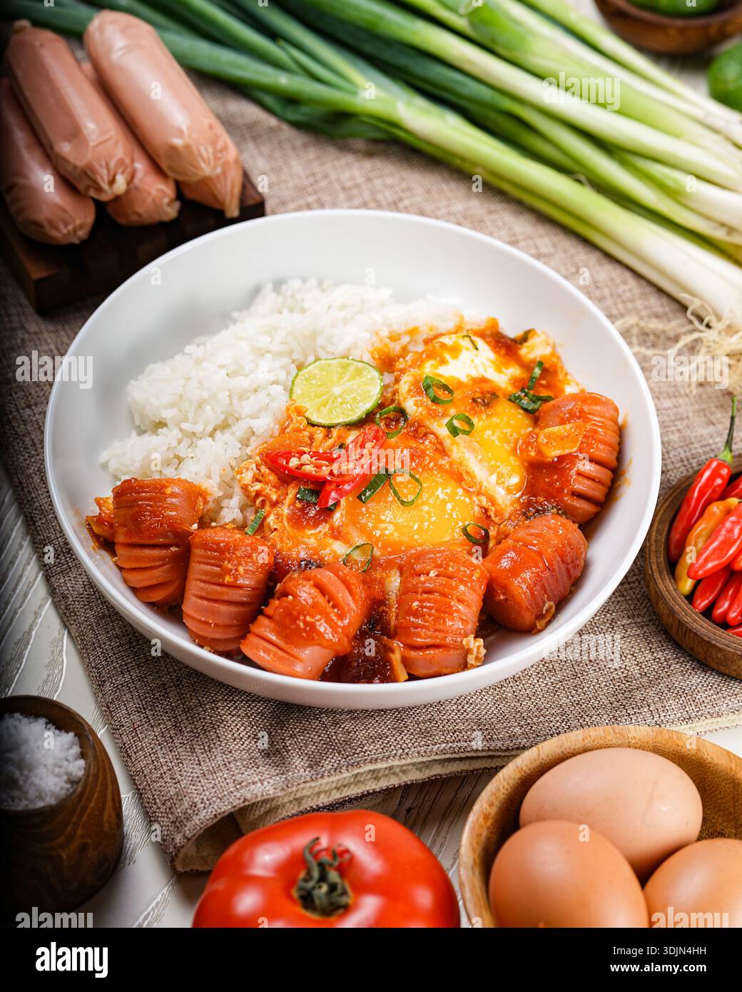 Assapora la mattina con un abbondante piatto di salsicce, uova fritte e riso fumante, guarnito con erbe fresche e peperoncino. Foto Stock