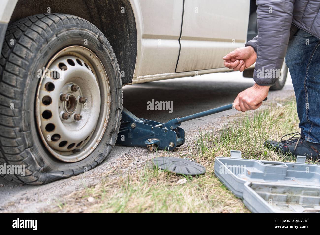 Assistenza stradale uomo cambio pneumatico forato con martinetto su auto in situazioni di emergenza Foto Stock