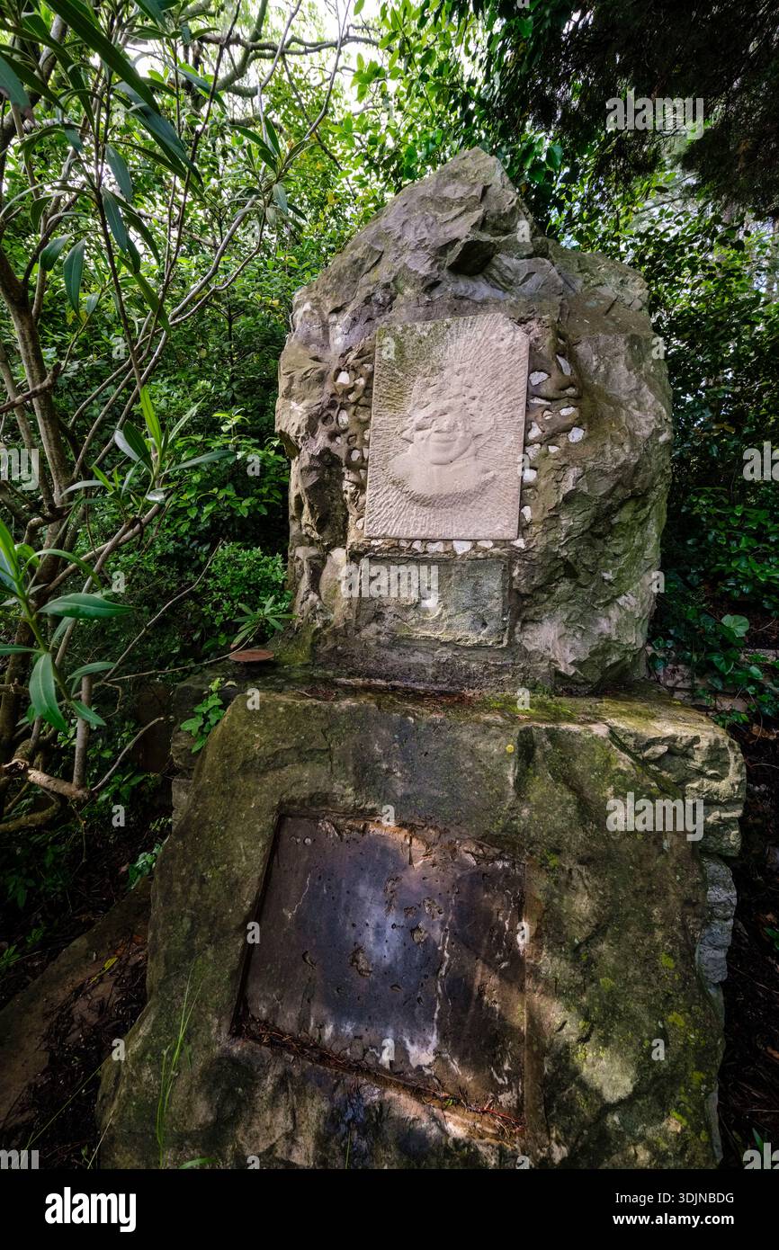 Monumento in pietra caratterizzato da un rilievo scolpito di un volto incastonato in una grande roccia, circondato da lussureggianti alberi verdi e cespugli in un ambiente simile a una foresta. Foto Stock