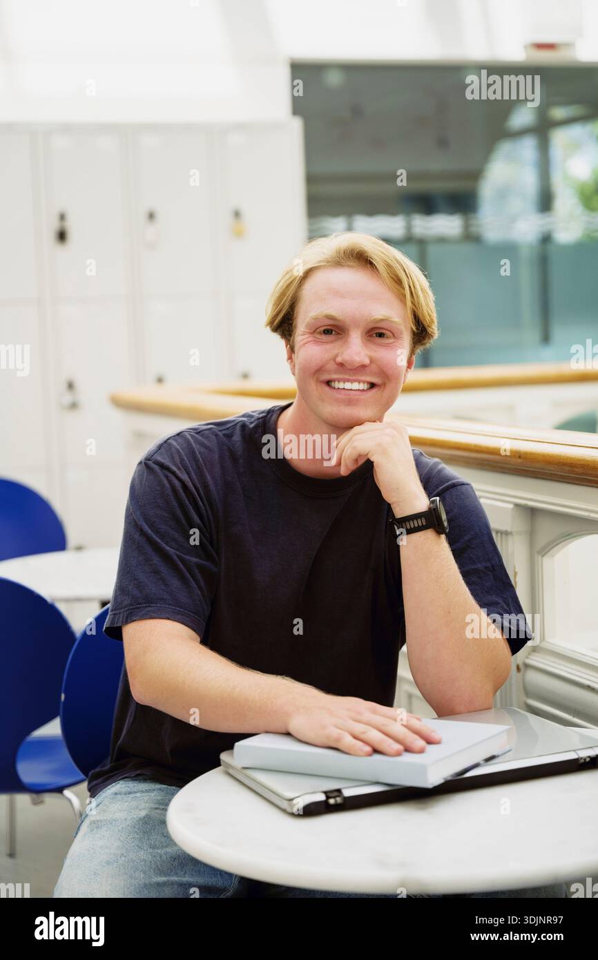 Ritratto di uno studente universitario sorridente seduto a un tavolo con materiale di studio nel campus Foto Stock