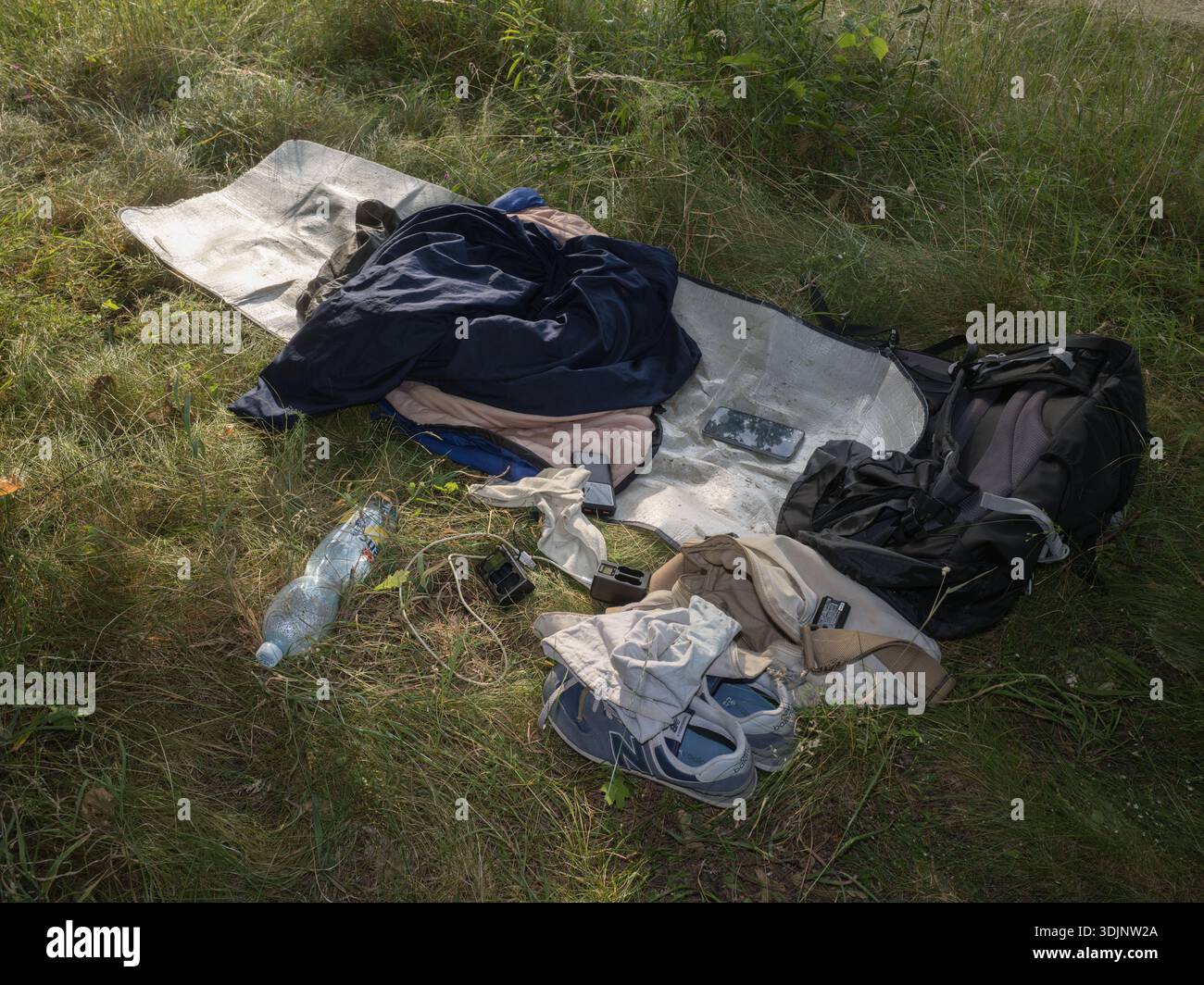Effetti personali, tra cui abiti, scarpe, uno zaino e una bottiglia d'acqua su un tappeto erboso Foto Stock
