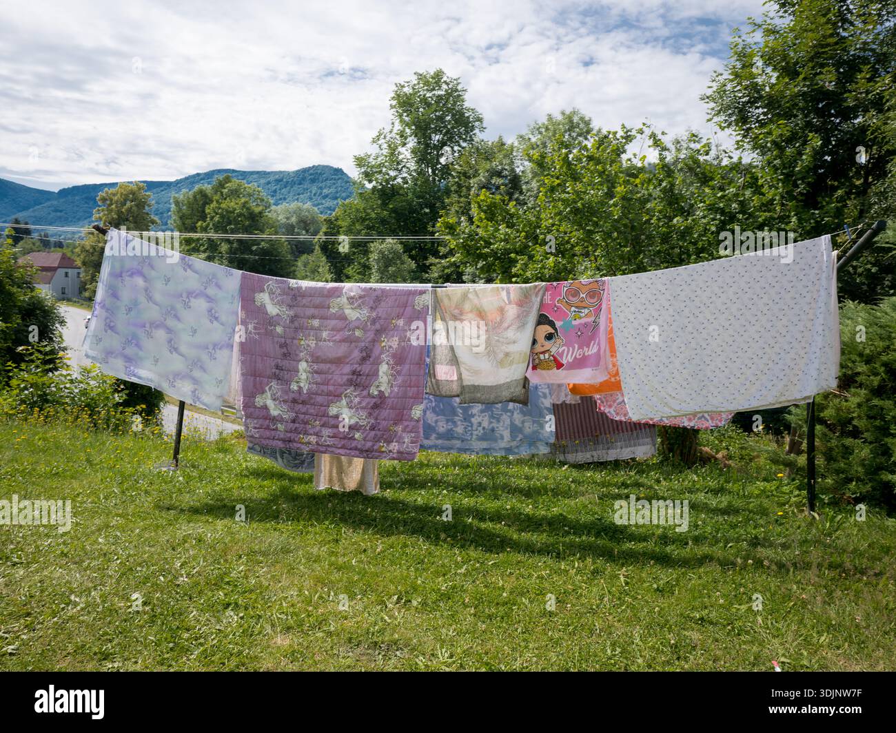 Varie coperte e lenzuola colorate appese su una lunga stoffa in un giardino erboso all'aperto Foto Stock