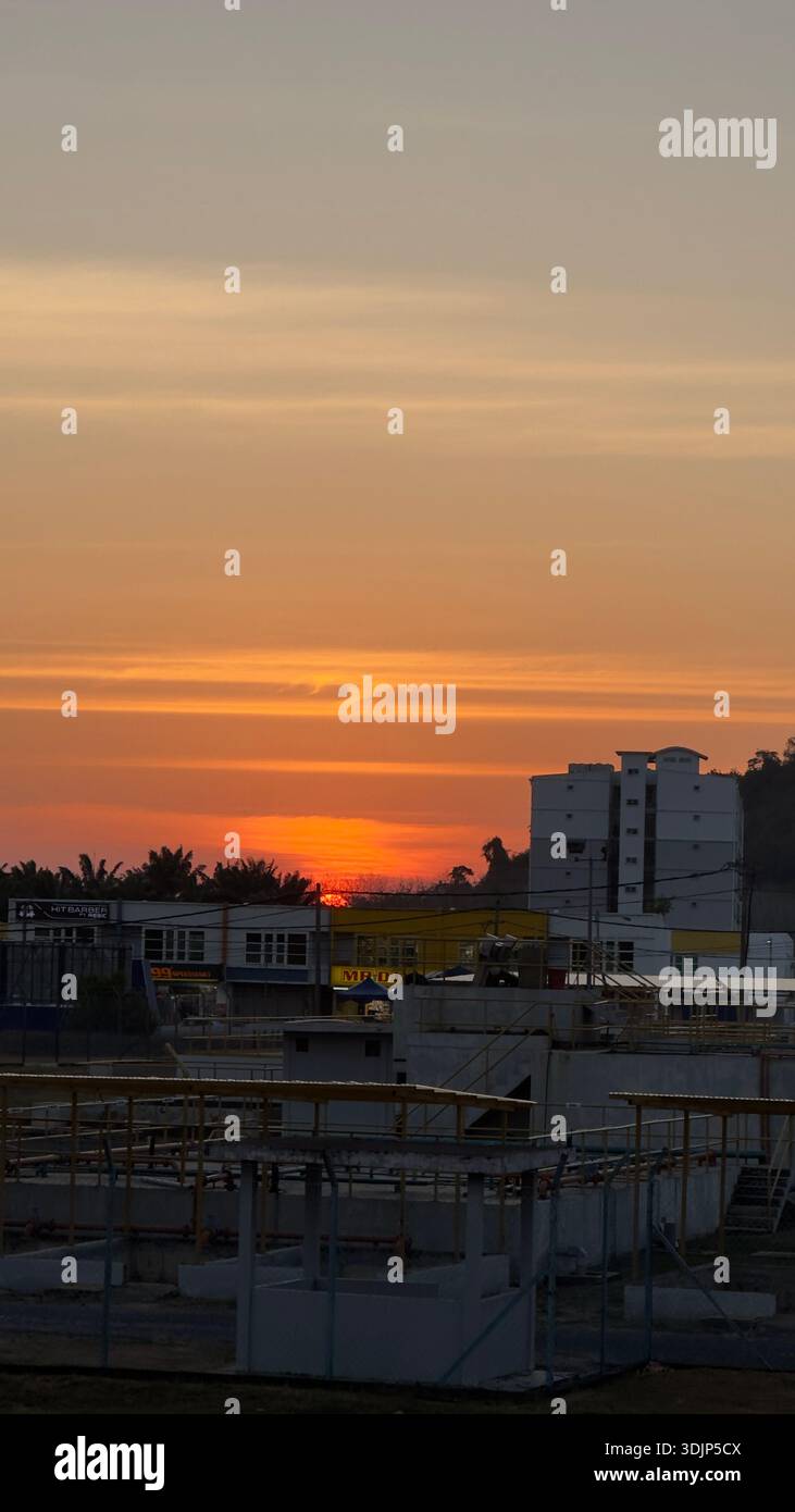 Il caldo tramonto giallo si illumina dietro gli edifici della città, proiettando una luce soffusa sui grattacieli, perfetto per temi urbani e architettonici - Immagine stock catturata con smartphone