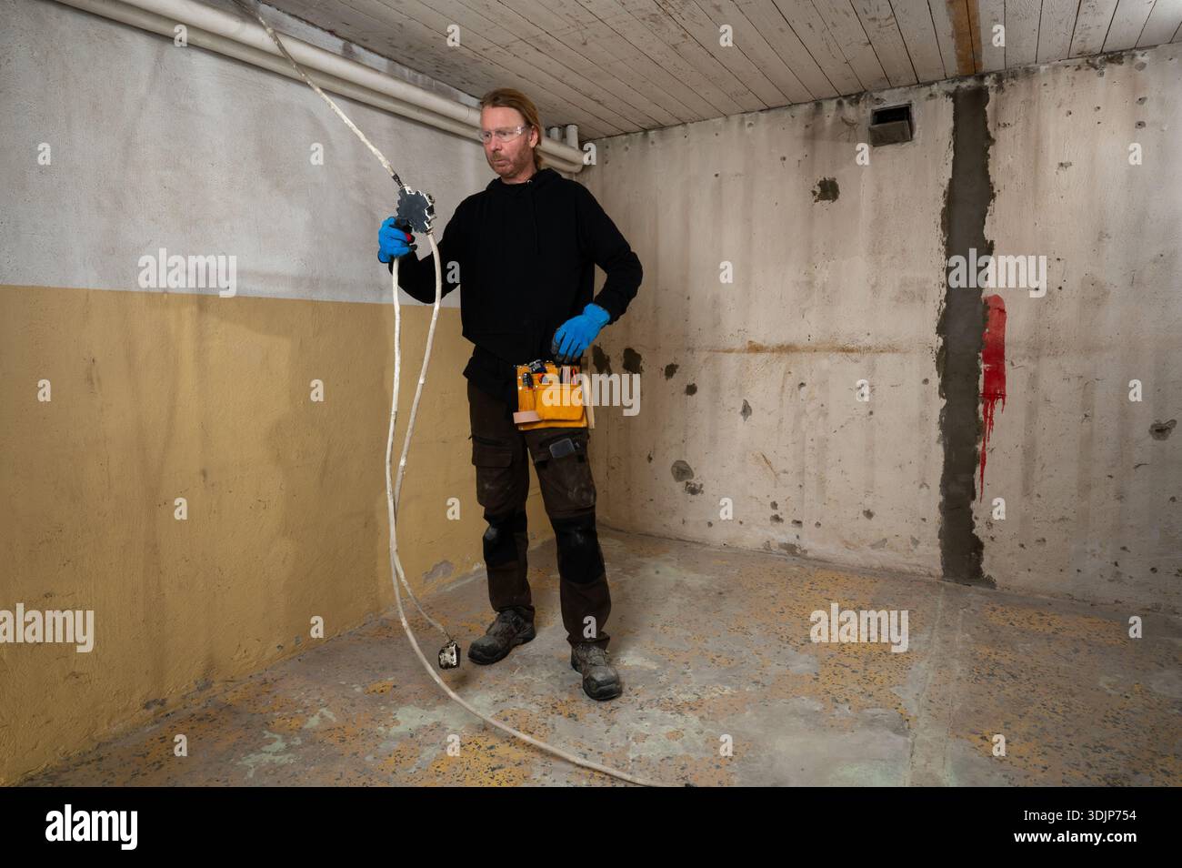 Elettricista che lavora con la scatola di derivazione elettrica e i cavi durante le ristrutturazioni interne, eseguendo un impianto elettrico professionale senza finitura Foto Stock