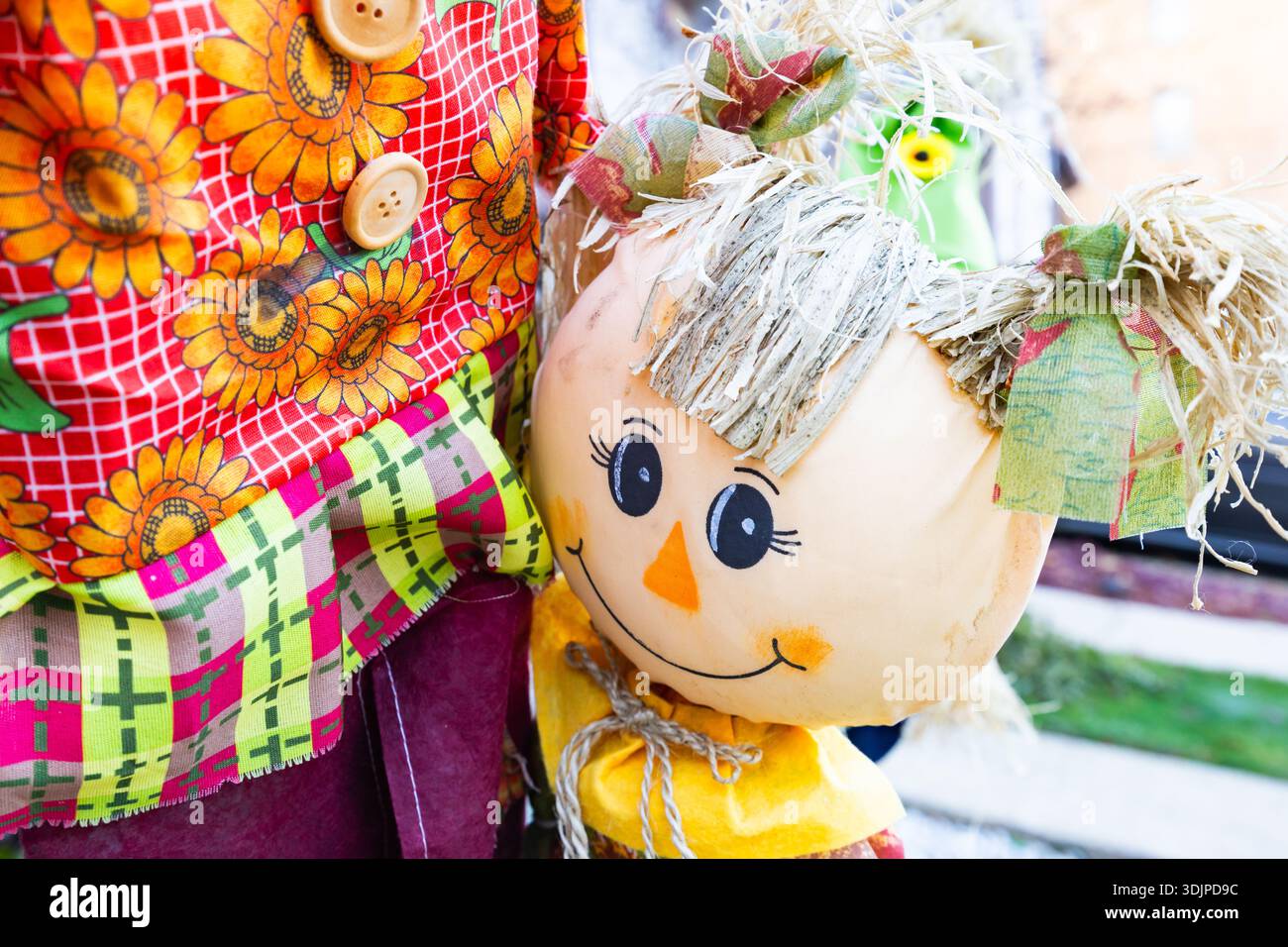 Primo piano di una bambola sorridente con capelli di paglia, abiti colorati in tessuto e tema autunnale, decorazioni autunnali all'aperto per il raccolto e Halloween Foto Stock