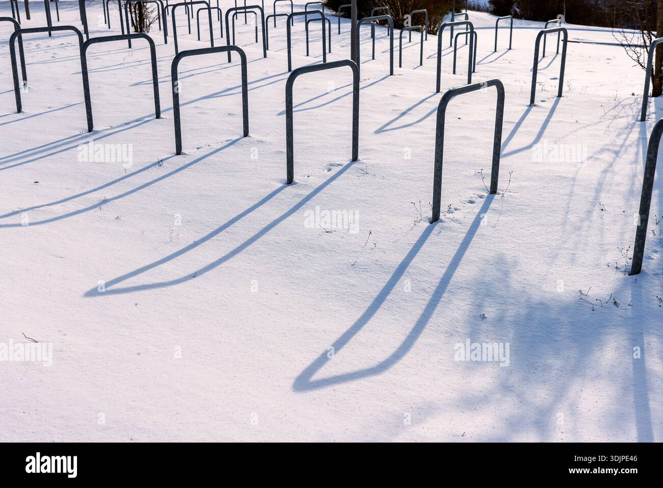 Parcheggio per biciclette coperto dalla neve con portabiciclette in metallo vuoto che getta lunghe ombre alla luce solare invernale. Foto Stock