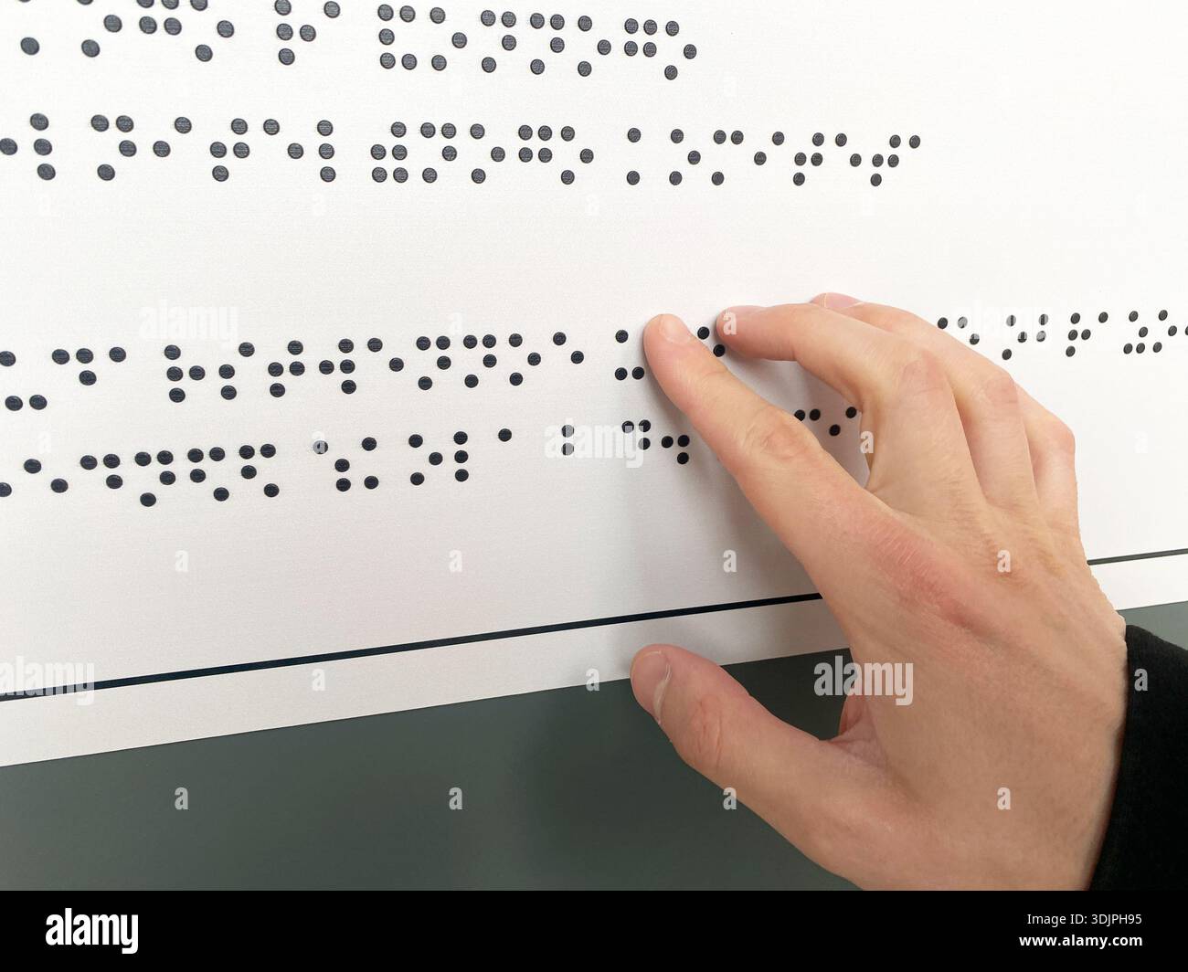 La mano interagisce con l'alfabeto Braille su una scheda tattile, progettata per la lettura da parte di persone non vedenti in un ambiente educativo Foto Stock