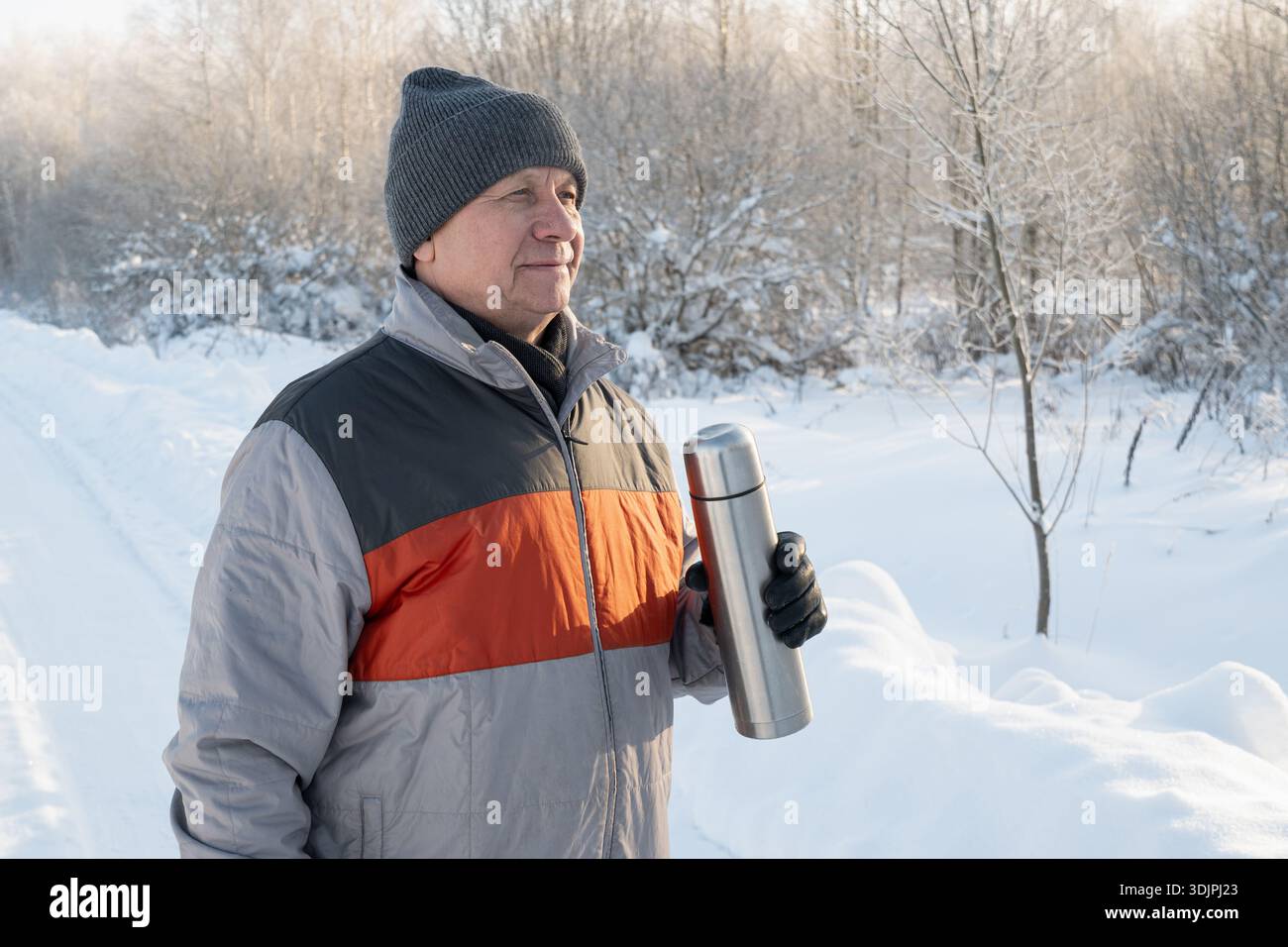 Un uomo adulto maturo tiene i termos metallici all'aperto in un ambiente invernale innevato. Uomo anziano che gusta una bevanda calda durante il freddo, lo stile di vita invernale e tu Foto Stock