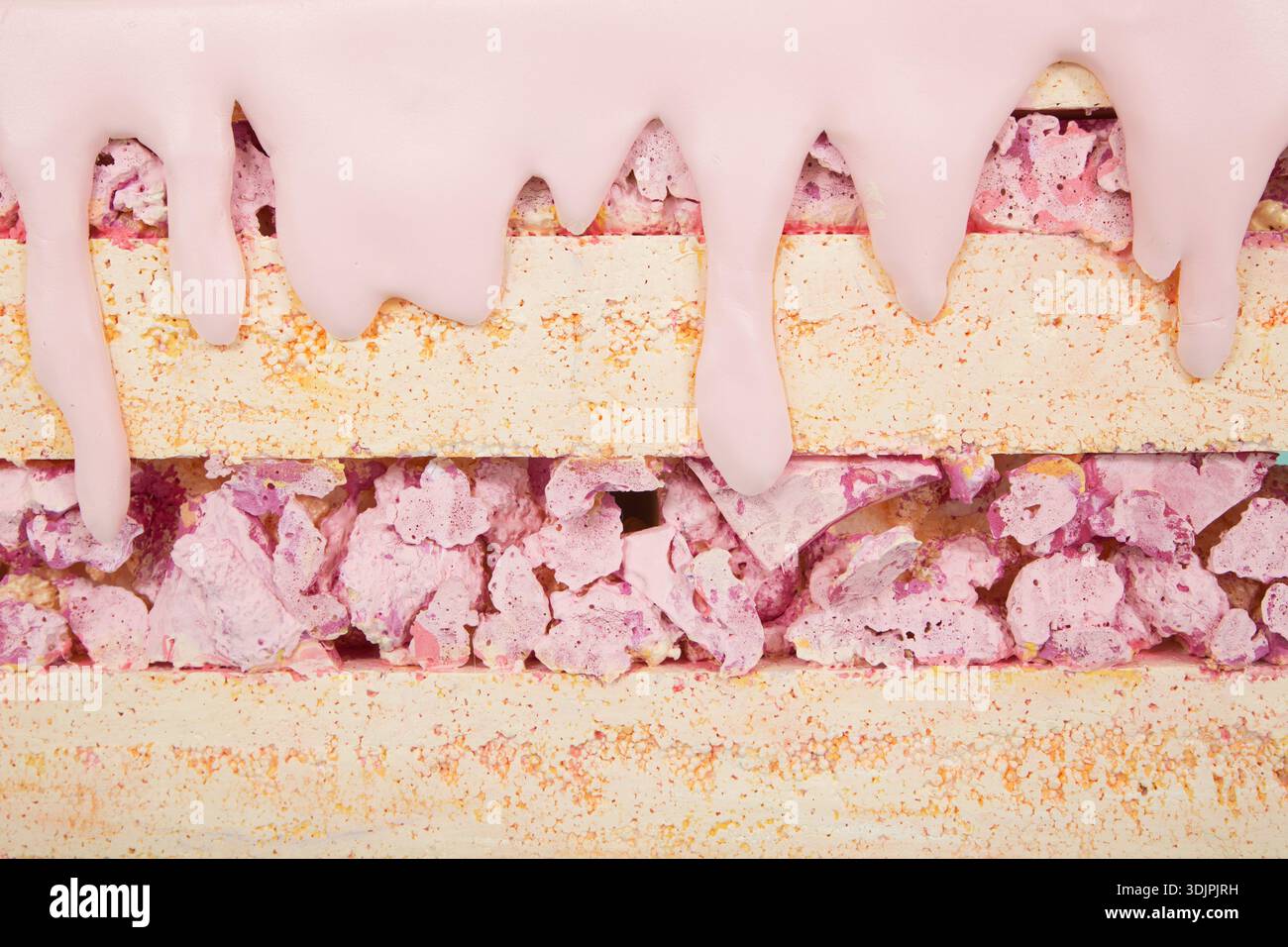Dolci artificiali realizzati in schiuma di polistirene, con strati di glassa rosa e colorate spruzzette, disposti su una superficie piana con un bac testurizzato Foto Stock