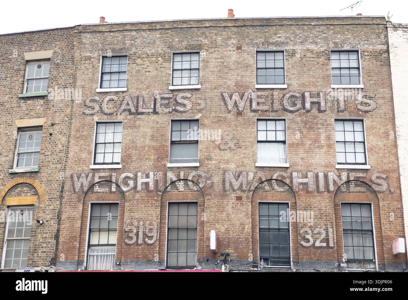 Insegna dipinta sbiadita con la scritta «Scales Weights & Weighers» su una facciata vittoriana di un edificio in mattoni a Londra Est, numerata 319-321. - Immagine stock catturata con smartphone