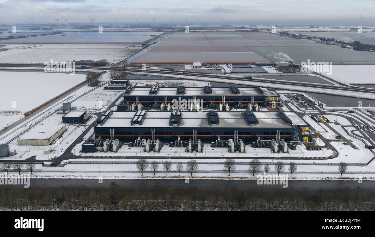 Veduta aerea di un paesaggio aspro e innevato, dove i datacenter Agriport si distinguono con le loro forme scure e geometriche contro l'espan piatto e bianco Foto Stock