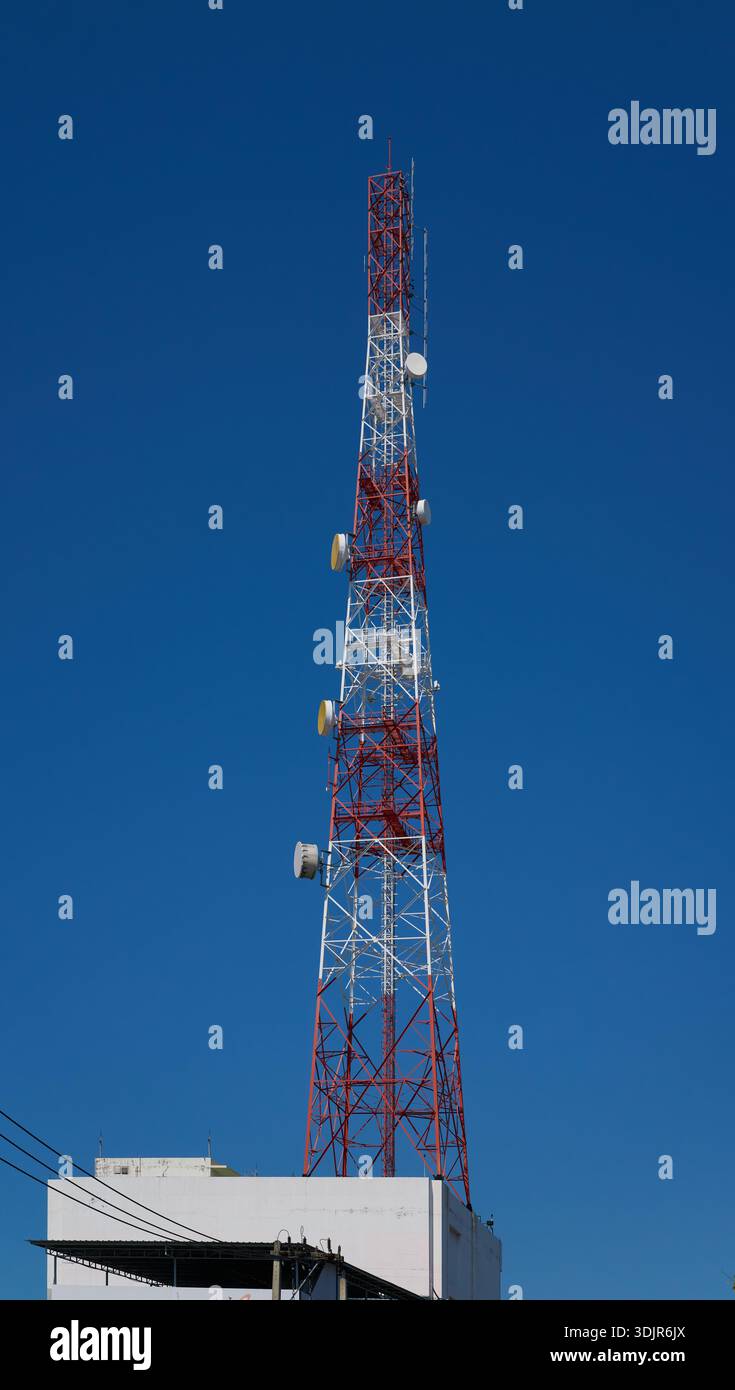 Alto torre di telecomunicazioni rossa e bianca con antenne a parabole contro un cielo blu limpido, edificio sul tetto, Thailandia Foto Stock