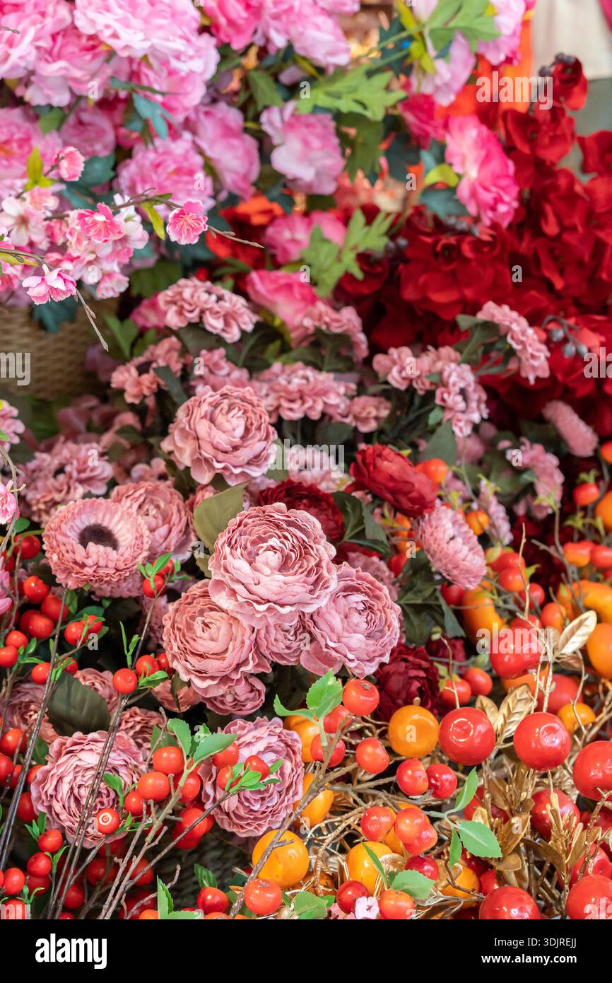 Rose rosa, garofani e peonie artificiali si mescolano con le bacche rosse brillanti e il lussureggiante fogliame in una vibrante composizione floreale. Foto Stock