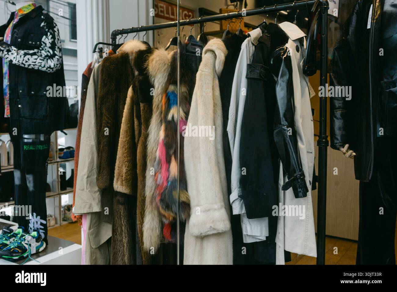 Una fila di vestiti è appesa su un rack. Stili e colori diversi sono visibili in un negozio. Gli acquirenti potrebbero curiosare nelle vicinanze. Foto Stock